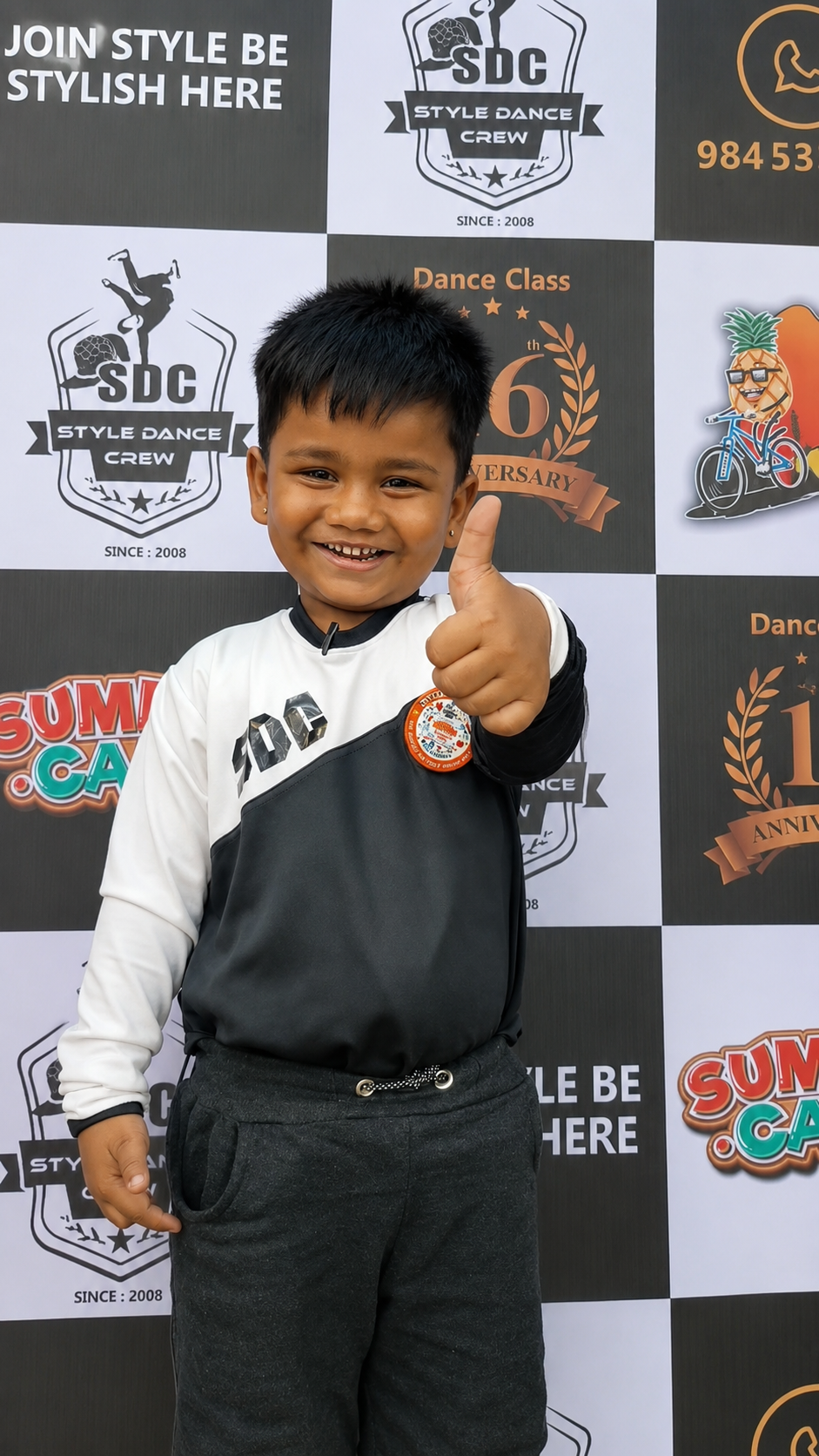 A young student in Style Dance Crew uniform holding a medal in front of the studio backdrop.